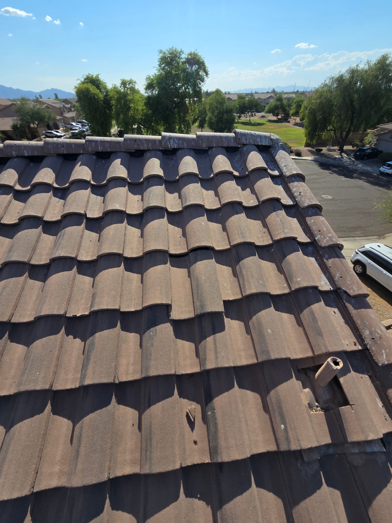 Overview of an aging concrete tile roof showing weathering and a damaged jack