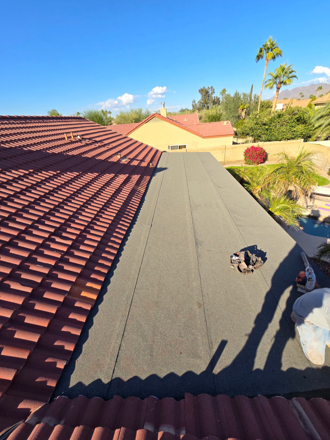 Long flat patio roof finished with granulated cap sheet beside red tile main roof