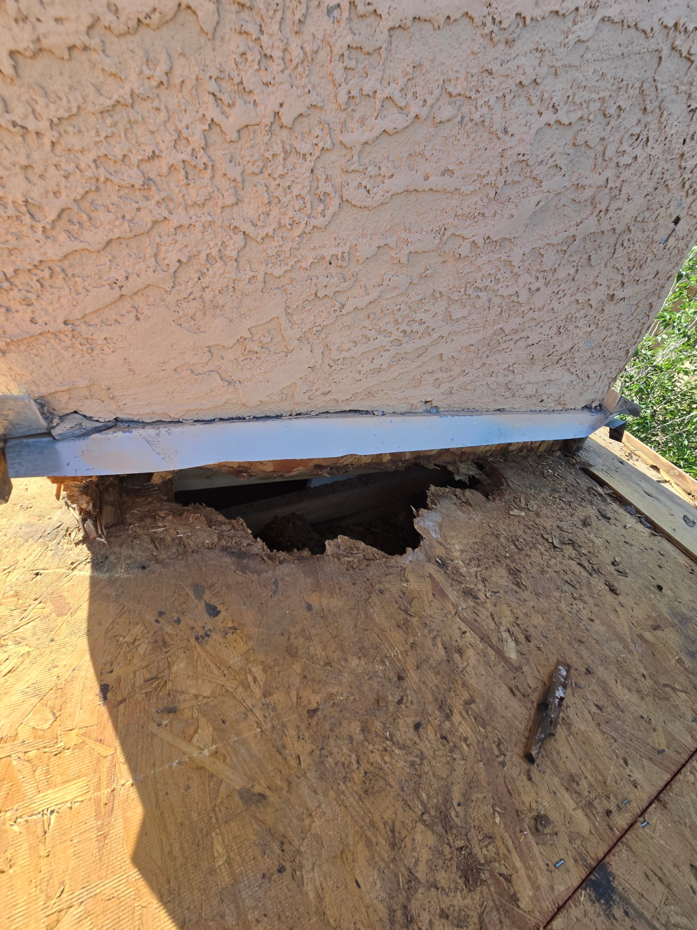 Rotted decking and damaged drip edge exposed under failed stucco flashing